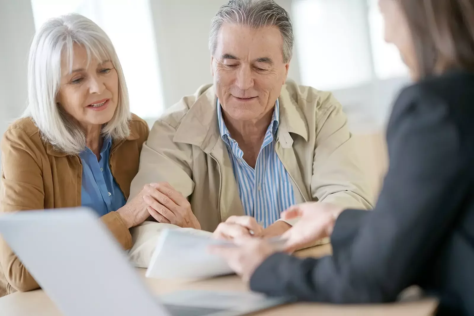 Senior couple sitting across from a professional, smiling while reviewing documents together.
